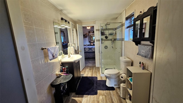 bathroom with tile walls, hardwood / wood-style floors, a shower with shower door, toilet, and vanity