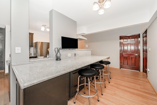 kitchen with light hardwood / wood-style flooring, stainless steel refrigerator, a kitchen breakfast bar, light stone countertops, and kitchen peninsula