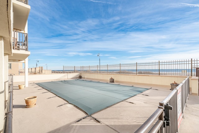 view of swimming pool with a water view, a beach view, and a patio