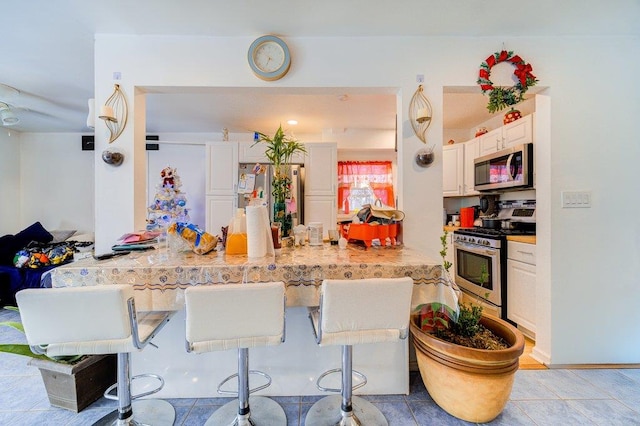 kitchen featuring kitchen peninsula, a kitchen breakfast bar, stainless steel appliances, and white cabinetry