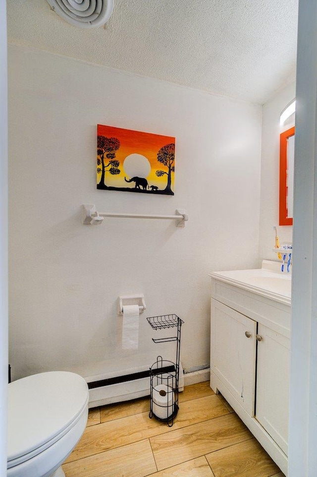 bathroom with wood-type flooring, a baseboard heating unit, vanity, and toilet