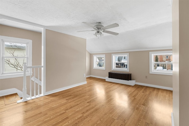 unfurnished living room with a wealth of natural light, a textured ceiling, light hardwood / wood-style floors, and radiator heating unit