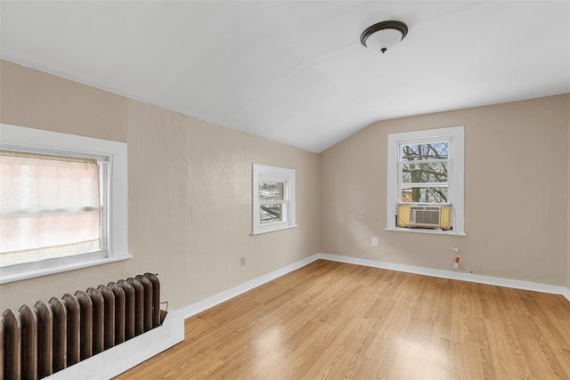 spare room with light hardwood / wood-style flooring, cooling unit, vaulted ceiling, and radiator