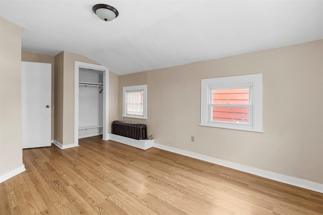 unfurnished bedroom featuring radiator, a closet, light wood-type flooring, and vaulted ceiling