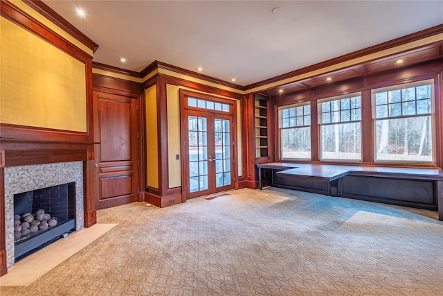 interior space with french doors, built in shelves, light colored carpet, a fireplace, and ornamental molding