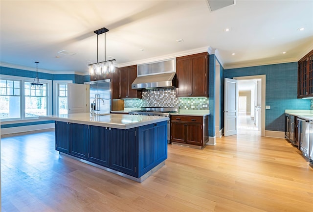 kitchen with light hardwood / wood-style floors, wall chimney range hood, premium appliances, and an island with sink