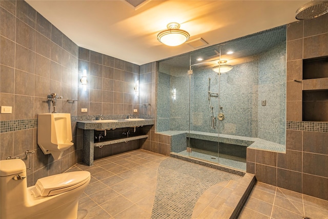 bathroom featuring tile patterned floors, tile walls, a shower with door, and dual sinks