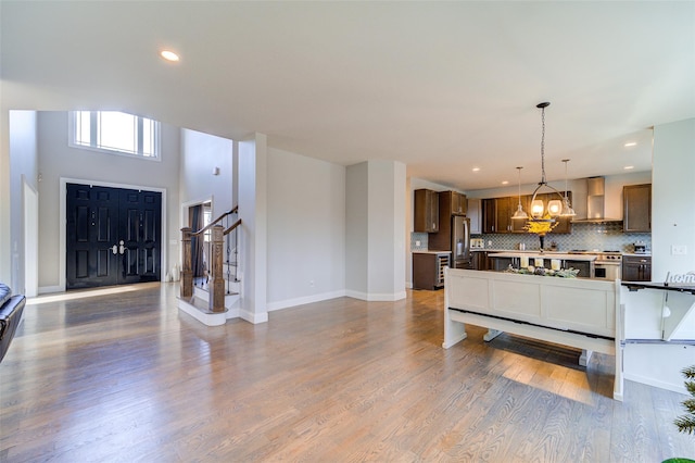 kitchen featuring appliances with stainless steel finishes, wall chimney exhaust hood, wood-type flooring, tasteful backsplash, and hanging light fixtures