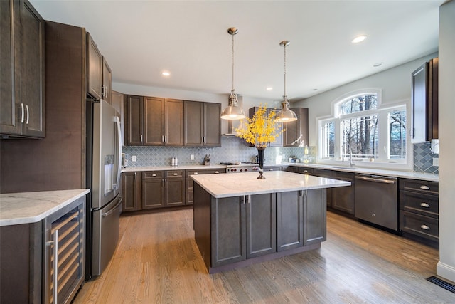 kitchen featuring an island with sink, appliances with stainless steel finishes, light wood-type flooring, wine cooler, and dark brown cabinetry