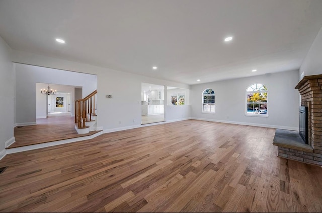 unfurnished living room featuring a brick fireplace, an inviting chandelier, and hardwood / wood-style floors