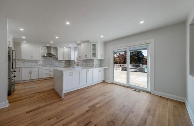 kitchen with sink, white cabinets, kitchen peninsula, light hardwood / wood-style flooring, and wall chimney range hood