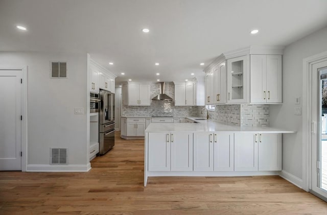 kitchen with sink, white cabinetry, light hardwood / wood-style flooring, kitchen peninsula, and wall chimney range hood