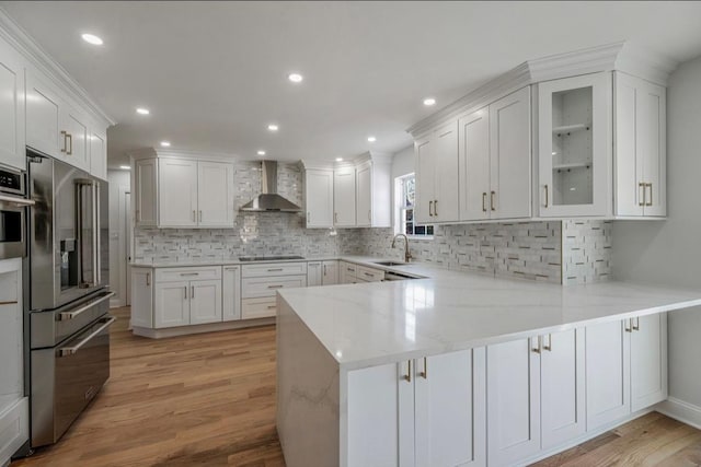 kitchen with sink, white cabinetry, wall chimney exhaust hood, light wood-type flooring, and kitchen peninsula