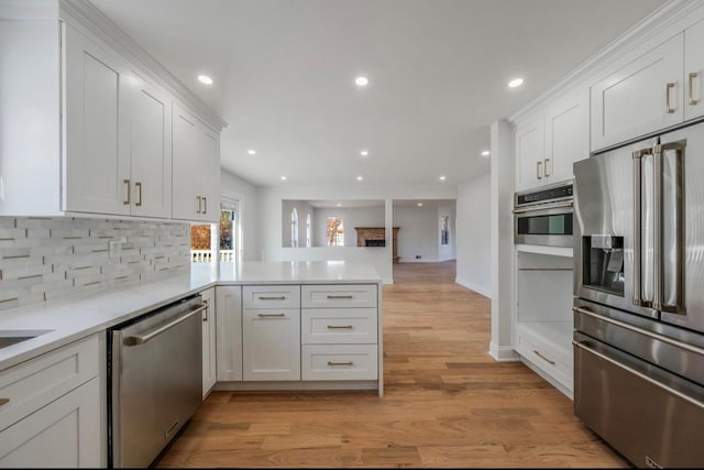 kitchen with kitchen peninsula, light wood-type flooring, backsplash, white cabinetry, and appliances with stainless steel finishes