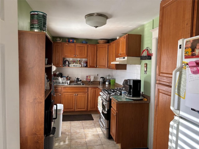 kitchen featuring sink, white refrigerator, light tile patterned floors, stainless steel gas range oven, and decorative backsplash