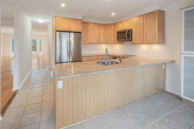 kitchen featuring kitchen peninsula, stainless steel appliances, light brown cabinetry, light stone counters, and sink