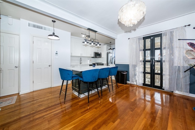 interior space with appliances with stainless steel finishes, white cabinetry, hanging light fixtures, hardwood / wood-style flooring, and a breakfast bar