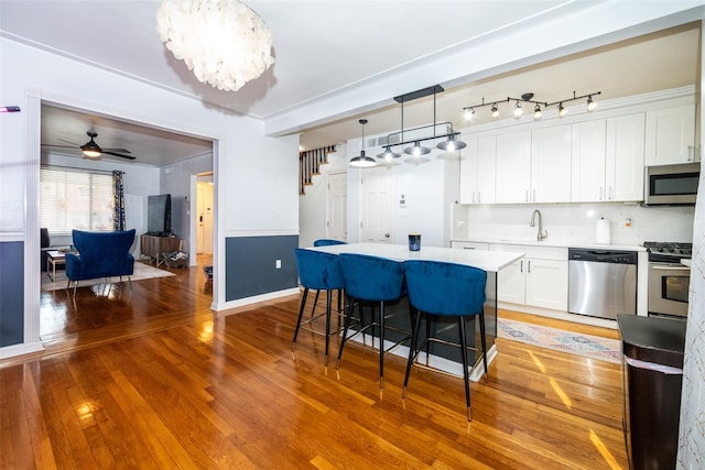 kitchen with appliances with stainless steel finishes, decorative light fixtures, wood-type flooring, white cabinets, and sink