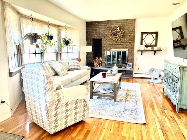 living room featuring a brick fireplace, light hardwood / wood-style flooring, plenty of natural light, and a baseboard radiator