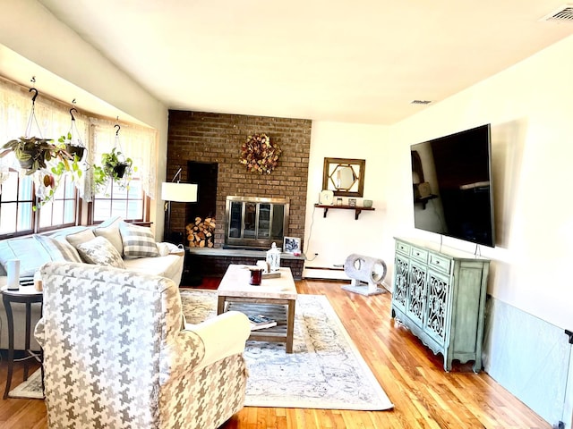 living room with light wood-type flooring, a fireplace, and a baseboard heating unit