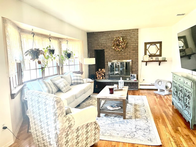 living area featuring visible vents, baseboards, wood finished floors, a brick fireplace, and a baseboard heating unit