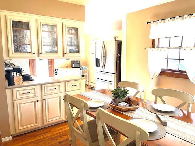 kitchen featuring cream cabinets, light wood-style flooring, light countertops, stainless steel fridge, and glass insert cabinets