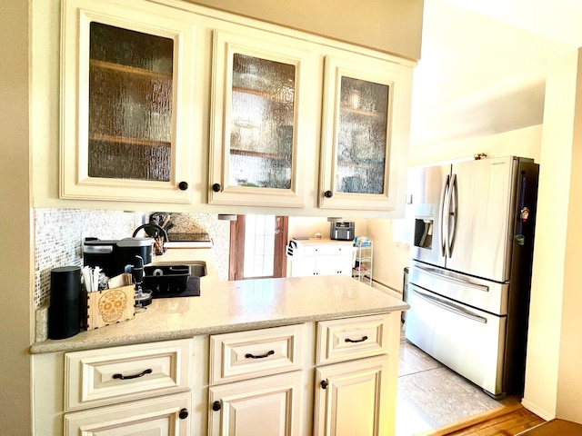 kitchen featuring light stone counters, cream cabinetry, stainless steel fridge, and glass insert cabinets