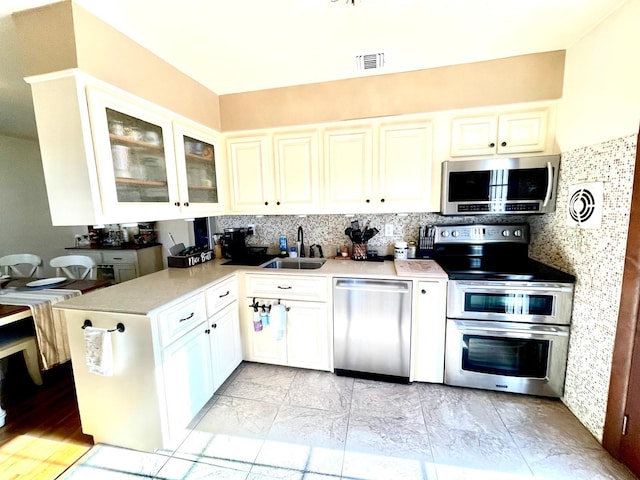 kitchen featuring a sink, visible vents, light countertops, appliances with stainless steel finishes, and glass insert cabinets