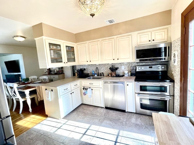 kitchen with stainless steel appliances, a sink, visible vents, light countertops, and tasteful backsplash