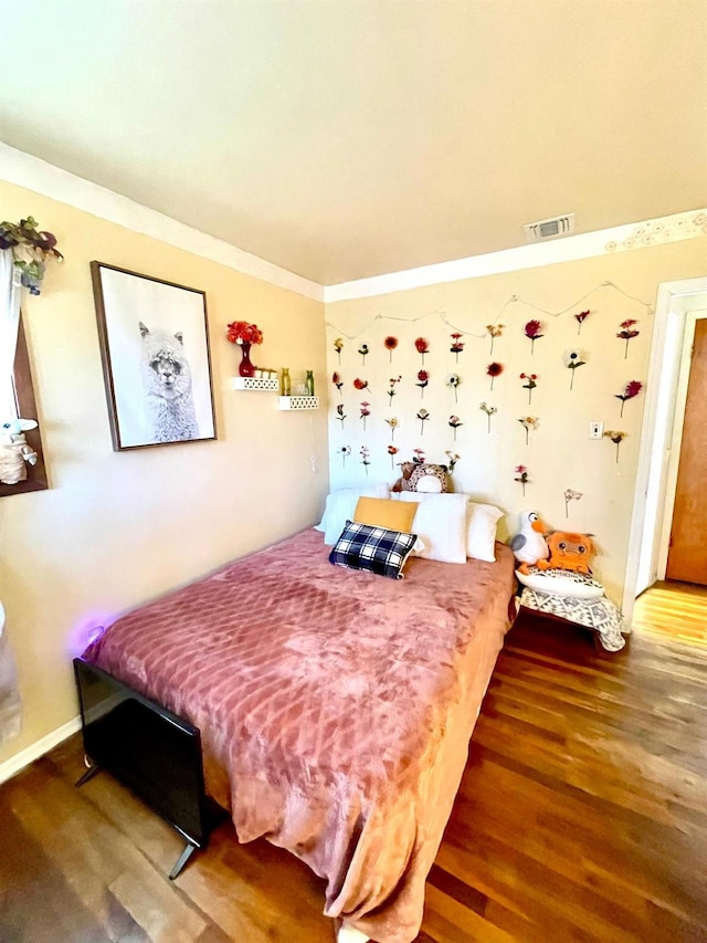 bedroom featuring crown molding, visible vents, and wood finished floors