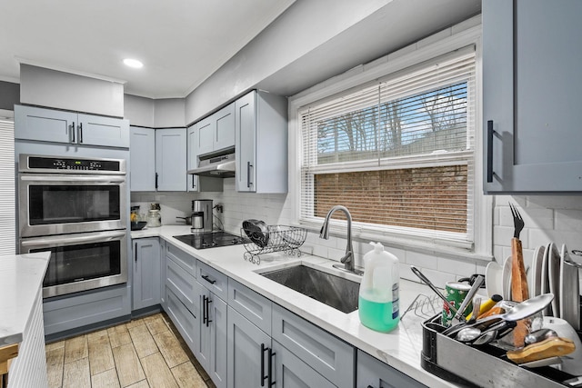 kitchen featuring black electric cooktop, decorative backsplash, gray cabinets, stainless steel double oven, and sink