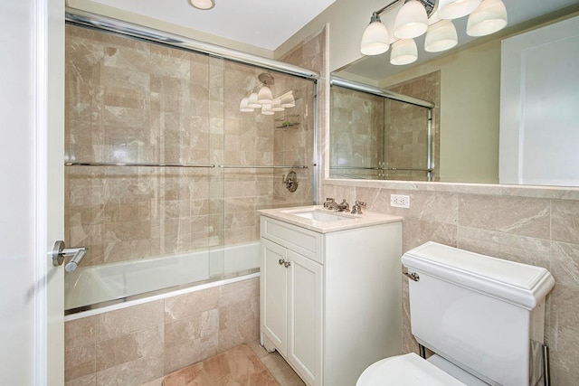 full bathroom with tile walls, vanity, bath / shower combo with glass door, and toilet