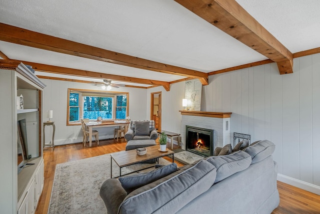 living room with a fireplace, light wood-type flooring, ceiling fan, and beamed ceiling