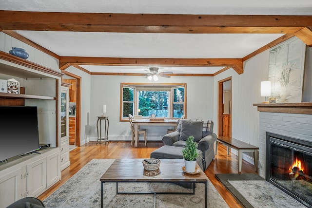 living room featuring beamed ceiling, a fireplace, ceiling fan, and light hardwood / wood-style floors