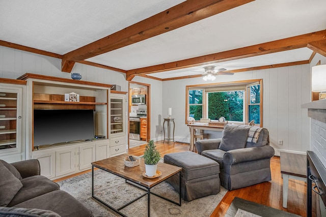 living room featuring light hardwood / wood-style flooring, wooden walls, a brick fireplace, beam ceiling, and ceiling fan