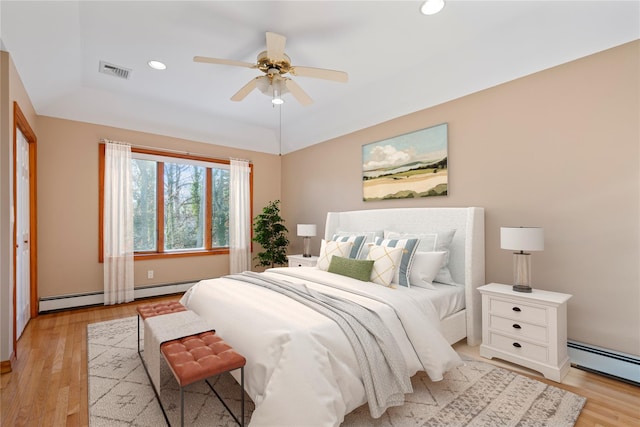 bedroom with a baseboard heating unit, a tray ceiling, light hardwood / wood-style floors, and ceiling fan