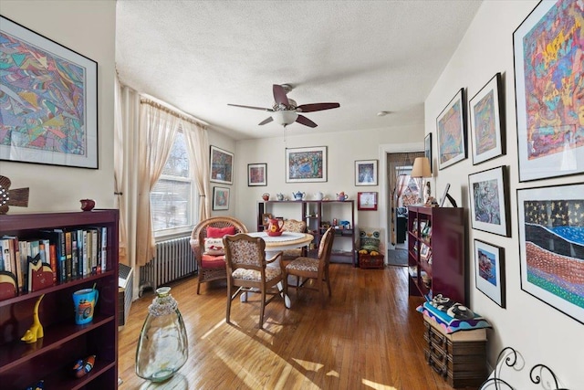 dining room with ceiling fan, wood-type flooring, radiator heating unit, and a textured ceiling