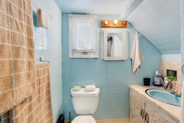 bathroom with toilet, vanity, vaulted ceiling, and tile walls