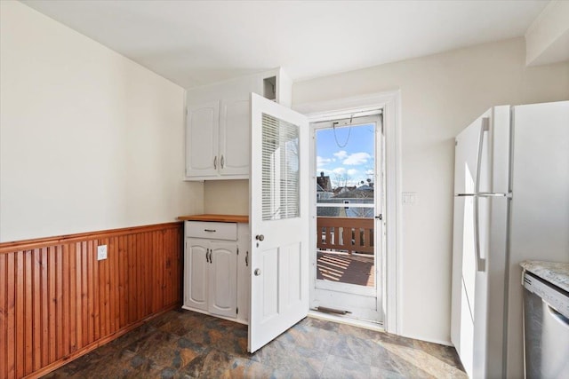 kitchen featuring white fridge, stainless steel dishwasher, white cabinets, and wooden walls