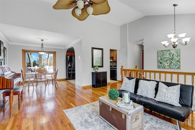 living room with ceiling fan with notable chandelier, vaulted ceiling, crown molding, and light hardwood / wood-style flooring