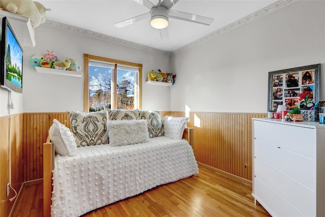 bedroom with ceiling fan, wooden walls, crown molding, and hardwood / wood-style flooring