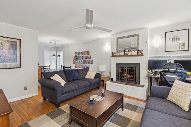 living room featuring ceiling fan with notable chandelier, a fireplace, ornamental molding, and light hardwood / wood-style floors