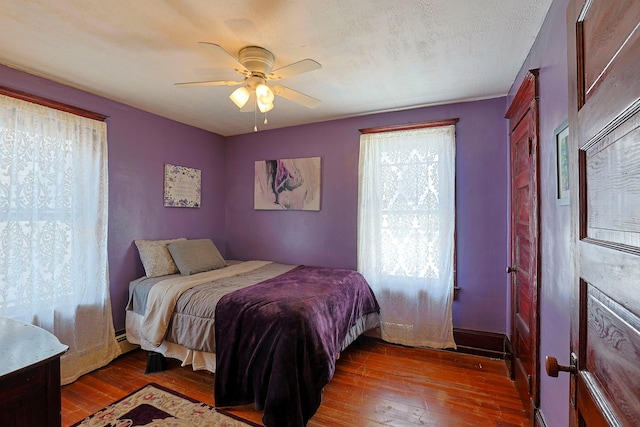 bedroom featuring ceiling fan, baseboard heating, a textured ceiling, and hardwood / wood-style flooring