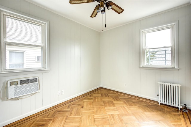 spare room featuring an AC wall unit, light parquet flooring, ornamental molding, ceiling fan, and radiator heating unit