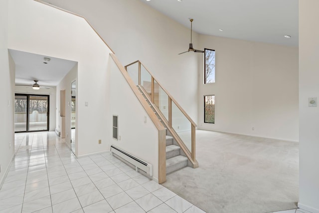 staircase with ceiling fan, baseboard heating, carpet flooring, and a high ceiling