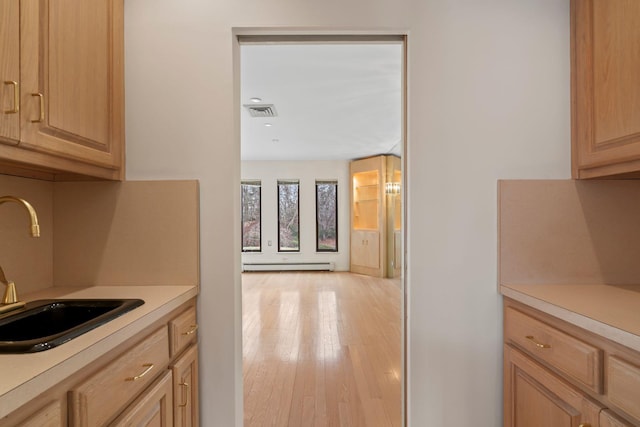 kitchen with sink, baseboard heating, light wood-type flooring, and light brown cabinetry