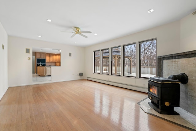 living room featuring baseboard heating, ceiling fan, light hardwood / wood-style floors, and a wood stove