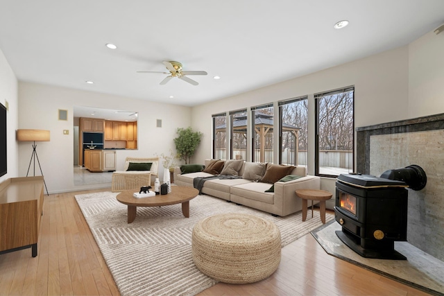 living room with light hardwood / wood-style floors, ceiling fan, and a wood stove