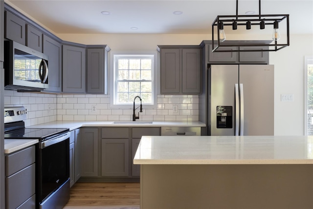 kitchen with light stone countertops, hanging light fixtures, stainless steel appliances, tasteful backsplash, and sink