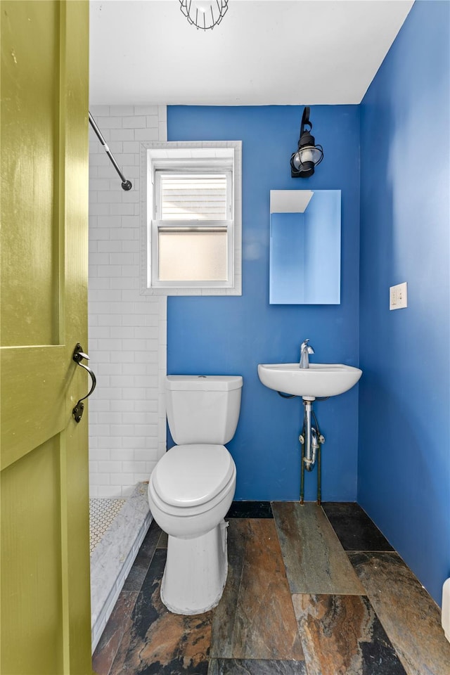 bathroom with sink, tiled shower, and toilet